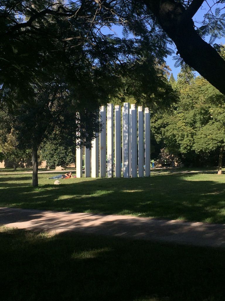 A group of rectangular white columns grouped together in the distance. A hanging tree branch in the foreground partially obscures the view.